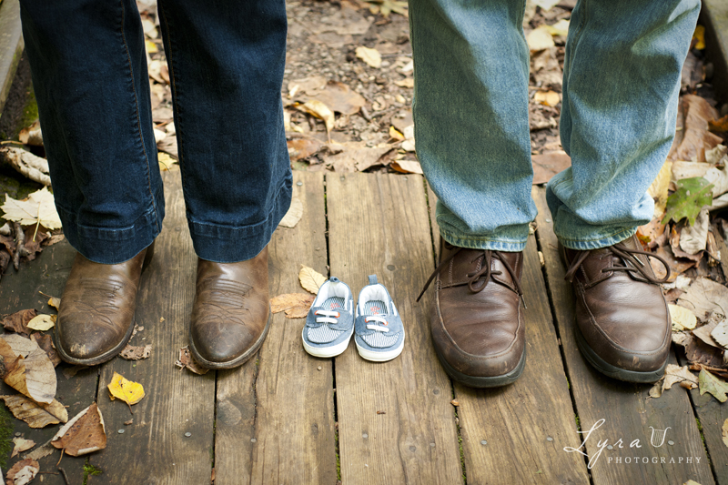 Baby shoes with expectant parents' feet on leafy trail